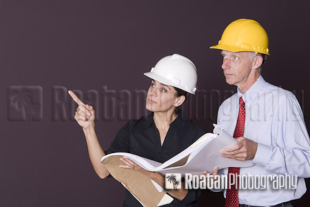 Two architects in hardhats examining blueprints